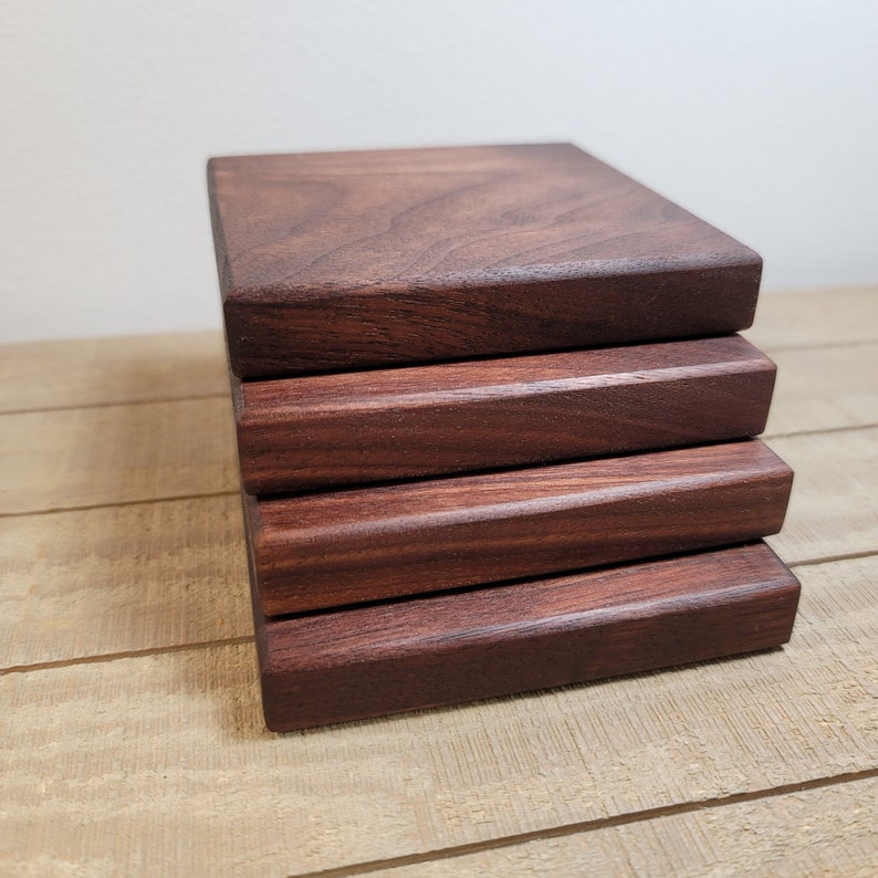 May include: A stack of five square wooden coasters made of dark walnut wood. The coasters are smooth and have a rich brown colour.