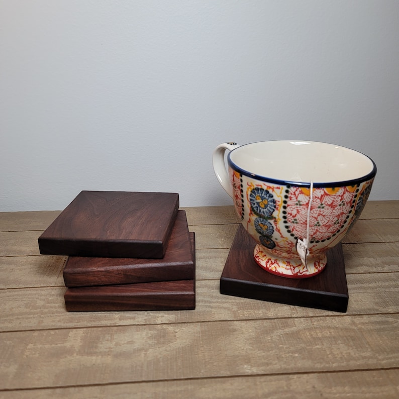 May include: Four dark brown wooden coasters stacked on top of each other. A colourful ceramic teacup with a floral design sits on a coaster.