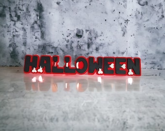 May include: Red and black Halloween sign with the word "HALLOWEEN" in black letters with white accents. The sign is sitting on a gray concrete surface.