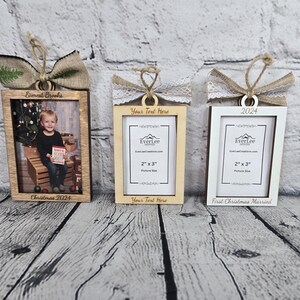 May include: Three wooden picture frame ornaments with burlap and lace bows. The frames are 2 inches by 3 inches and can hold a 2x3 inch photo. The first frame says "Everest Brooks Christmas 2024" and has a photo of a young boy in it. The second frame says "Your Text Here" and the third frame says "2024 First Christmas Married".