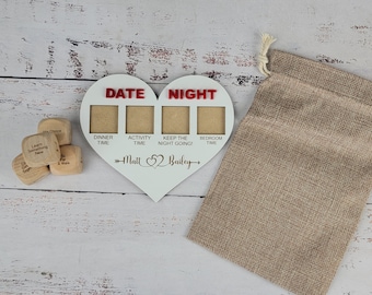 May include: White wooden heart-shaped frame with the words "Date Night" and four blank spaces for photos. The frame has the words "Dinner Time", "Activity Time", "Keep the Night Going!" and "Bedroom Time" written below the photo spaces. The frame also has the names "Matt" and "Bailey" written below the photo spaces. There are four wooden dice with different phrases written on them.