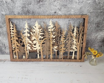 Könnte beinhalten: Ein Wandbild aus Holz, das eine Waldszene mit mehreren Bäumen darstellt. Die Bäume sind aus dem Holz ausgeschnitten, wodurch ein geschichteter Effekt entsteht. Das Stück ist in einem dunkelbraunen Holzrahmen gerahmt.