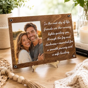 May include: A rectangular wooden photo frame featuring a photograph of a smiling couple on the left and the text "In the vast sky of life, friends are the runway lights guiding you through the fog and darkness—essential for a smooth journey and a safe landing" on the right.