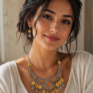 Peut inclure: Un collier imposant en métal argenté orné d'émaux orange, de perles jaunes et de breloques en forme de main de Hamsa, accompagné de boucles d'oreilles assorties composées d'une perle jaune et d'une petite main de Hamsa en argent.