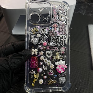 May include: A clear phone case with a glittery, pink, and white design. The case is filled with various charms, including hearts, stars, butterflies, and a pink and white checkered hat. The name "Jaso" is spelled out in gold letters on the case.