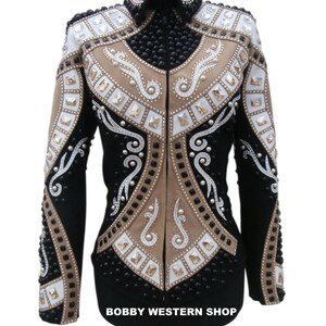 May include: A black, tan, and white long-sleeve jacket featuring a high collar, front zip, and intricate embellishments including black studs, clear crystals, and white scrollwork patterns. The text BOBBY WESTERN SHOP is printed at the bottom.
