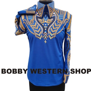 May include: A bright blue long-sleeve shirt featuring an intricate chest and collar design with gold, light blue, and dark brown beadwork, metallic accents, and clear crystals. The text BOBBY WESTERN SHOP is printed in black across the lower section.