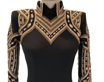 Puede incluir: Una camisa negra de manga larga con cuello alto y adornos intrincados de cristales dorados, plateados y transparentes dispuestos en patrones geométricos en los hombros y el pecho. El texto BOBBY WESTERN SHOP aparece impreso en blanco abajo.