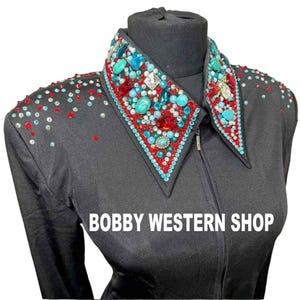 Könnte beinhalten: Ein schwarzes Langarmshirt mit einem spitzen Kragen, der reich mit türkisfarbenen Steinen, roten Kristallen und klaren Strasssteinen verziert ist. Die Schultern sind mit einem Streumuster aus roten und türkisfarbenen Kristallen besetzt. Text: BOBBY WESTERN SHOP.