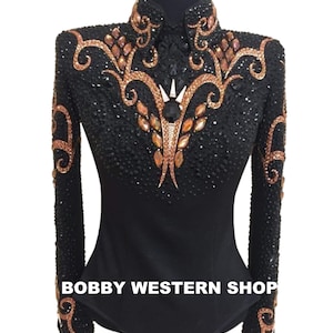 Pode incluir: Uma camisa preta de manga comprida com gola alta, adornada com padrões intrincados de cristais cor de cobre e missangas pretas densas. O texto BOBBY WESTERN SHOP está impresso a branco na parte inferior frontal da peça.