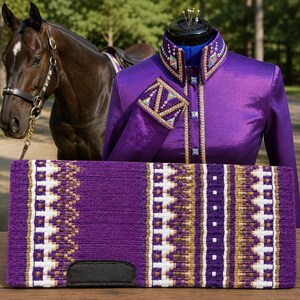 Könnte beinhalten: Eine violette Pferdesatteldecke mit geometrischem Muster in Weiß und Gold, präsentiert neben einem passenden violetten Langarm-Turniershirt mit Goldbesatz, Kristallverzierungen an Kragen und Manschetten sowie einem dunkelbraunen Pferd.
