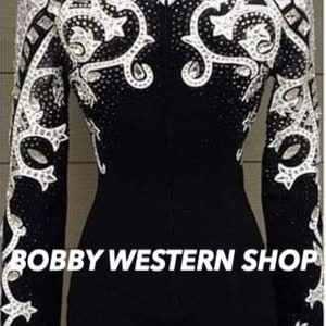 May include: Black equestrian show jacket with intricate white and silver embellishments. The jacket features a high collar and long sleeves, with ornate patterns of rhinestones and decorative elements. The text "BOBBY WESTERN SHOP" is visible at the bottom.