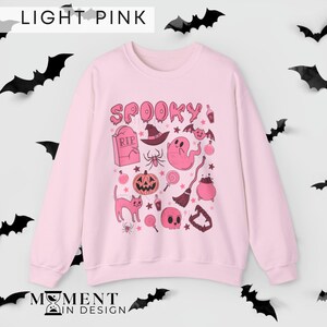 pink aesthetic halloween sweatshirt for women. contains pink graphics of ghosts, pumpkins, cats, potions, and candy.