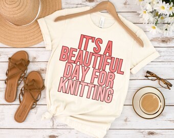 May include: A white t-shirt with the text "It's a beautiful day for knitting" in pink and red lettering.