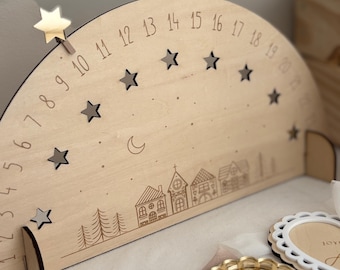 Puede incluir: Calendario de Adviento navideño de madera en forma de semicírculo, con números grabados, estrellas, una luna y una escena de pueblo. Se adjunta un clip de estrella dorada. Se ven piezas decorativas de madera adicionales.