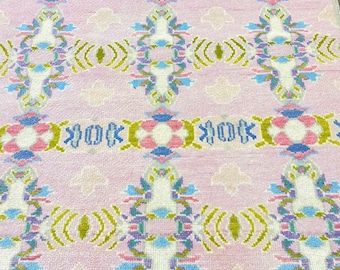 May include: A pink and white rug with a geometric pattern in shades of blue, green, and yellow. The rug has a traditional design with repeating motifs.