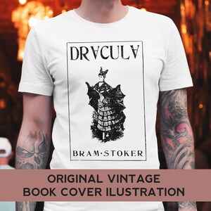 May include: A white t-shirt with a black and white illustration of a woman in a dress with bat wings. The text "DRACULA" and "BRAM STOKER" are printed on the shirt.