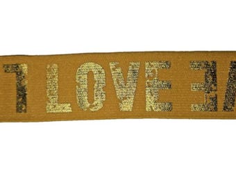 May include: A tan fabric strip with the word "LOVE" printed in a distressed gold font. The letters have a textured, worn appearance, creating a vintage aesthetic. The background is a solid tan color.