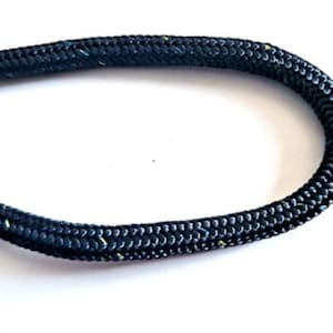 Puede incluir: Primer plano de una cuerda azul oscuro con una textura trenzada y pequeñas motas amarillas y azules. La cuerda está curvada sobre un fondo blanco. Ideal para proyectos de artesanía o náuticos, la textura de la cuerda es visible.
