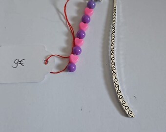 May include: A silver bookmark with a heart-shaped design and a string of pink and purple heart-shaped beads.