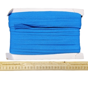 Pode incluir: Um rolo de cordão elástico azul brilhante, com aproximadamente 76 cm de comprimento, é exibido em um carretel de papelão branco. Uma régua de madeira com o texto "Dragonpandakreativ" e os números de 1 a 30 é colocada abaixo do carretel.