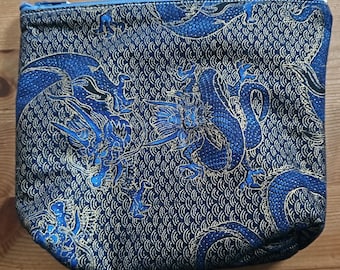 May include: A blue and gold zippered pouch with a dragon pattern. The pouch is made of a fabric with a woven texture.
