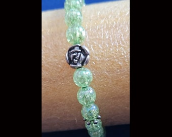 May include: A green beaded bracelet with a silver rose charm. The beads are small and have a sparkly finish.