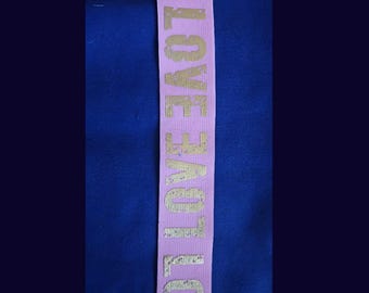 Könnte beinhalten: Rosa elastisches Band mit dem Wort "LOVE" in Gold gedruckt.