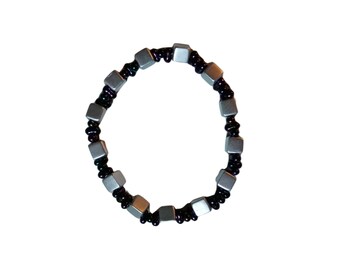 Puede incluir: Un brazalete de cuentas plateadas y negras con cuentas de forma cuadrada.