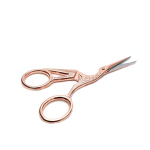 May include: Rose gold scissors with a bird design. The scissors have two oval-shaped blades and a decorative handle.