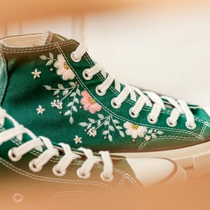 May include: A pair of green canvas high-top sneakers with white laces and embroidered floral designs.