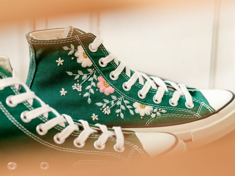 May include: A pair of green canvas high-top sneakers with white laces and embroidered floral designs.