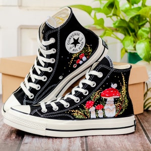 May include: A pair of black high-top Converse sneakers with white soles. The sneakers are decorated with embroidered mushrooms and greenery.