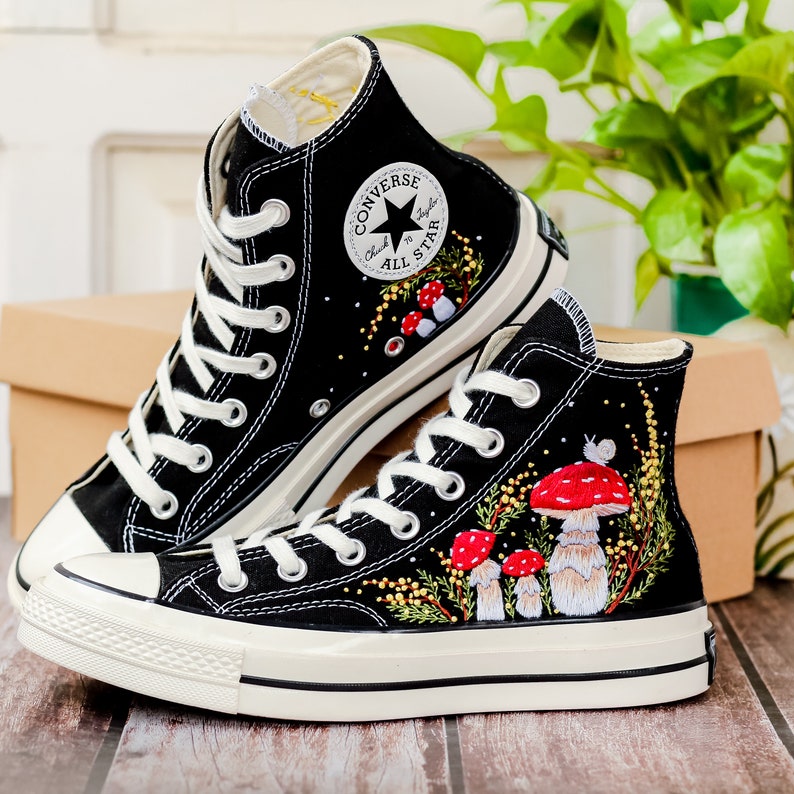 May include: A pair of black high-top Converse sneakers with white soles. The sneakers are decorated with embroidered mushrooms and greenery.
