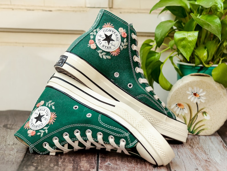 May include: A pair of green high-top Converse sneakers with white soles and floral embroidery. The sneakers feature a black star logo with the text "Converse All Star" on the side.