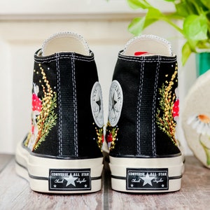 May include: Black high-top Converse sneakers with embroidered mushrooms and greenery. The sneakers have a white rubber sole and the Converse All Star logo is visible on the back.