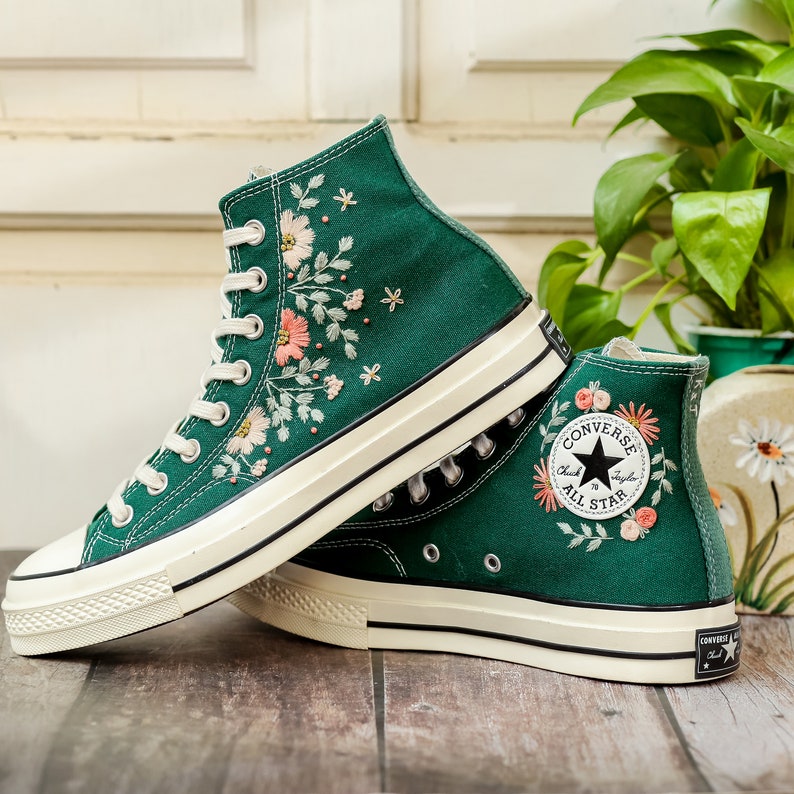 May include: Green high-top Converse sneakers with embroidered floral details and a white rubber sole. The Converse logo is visible on the side of the shoe.