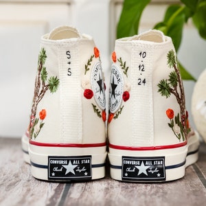 May include: A pair of white high-top Converse sneakers with embroidered floral designs and the text "5+5" and "10.12.24" on the back.
