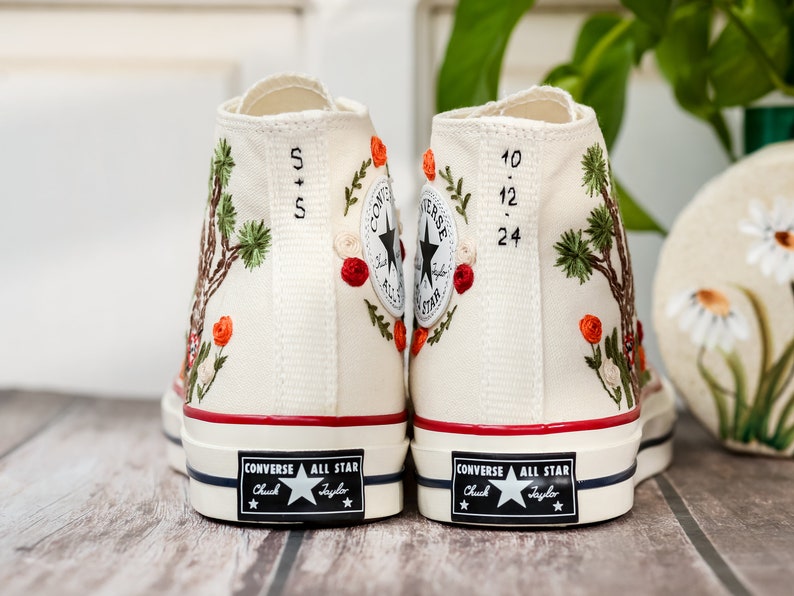 May include: A pair of white high-top Converse sneakers with embroidered floral designs and the text "5+5" and "10.12.24" on the back.