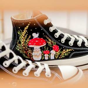 May include: Black high-top canvas sneakers with embroidered red and white mushrooms and yellow flowers.