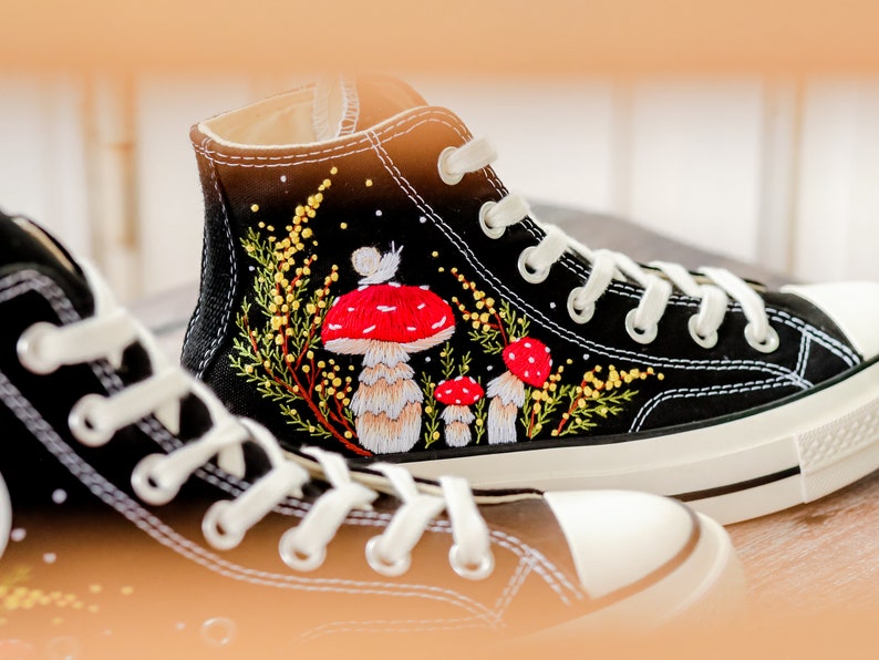 May include: Black high-top canvas sneakers with embroidered red and white mushrooms and yellow flowers.