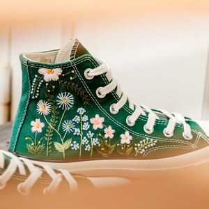 Puede incluir: Zapatillas altas verdes con cordones blancos y puntera blanca. Las zapatillas est&aacute;n adornadas con flores bordadas en tonos rosas, blancos y azules, con hojas verdes y detalles amarillos. El dise&ntilde;o floral est&aacute; en el lateral del zapato.