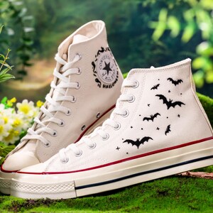 以下が含まれることがあります： 黒のバットのデザインと側面に「Converse All Star Halloween」の文字が書かれた、白いハイカットのコンバーススニーカーのペアです。