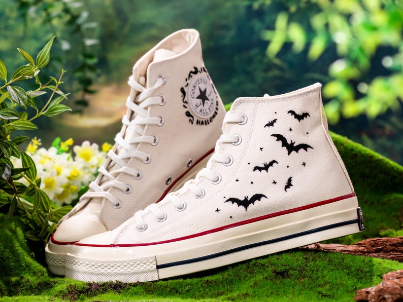 以下が含まれることがあります： 黒のバットのデザインと側面に「Converse All Star Halloween」の文字が書かれた、白いハイカットのコンバーススニーカーのペアです。