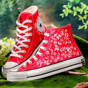 Puede incluir: Zapatillas Converse rojas de caña alta con diseños navideños bordados en blanco, incluyendo copos de nieve, acebo y adornos.