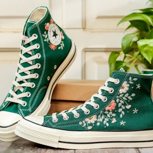 May include: A pair of green high-top canvas sneakers with white soles and embroidered floral designs. The sneakers have white laces and a white star logo on the side.