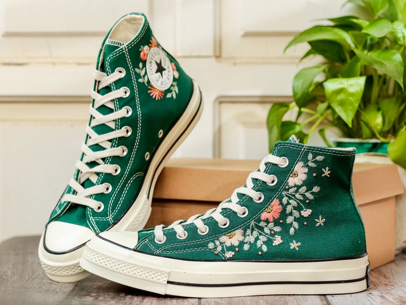 May include: A pair of green high-top canvas sneakers with white soles and embroidered floral designs. The sneakers have white laces and a white star logo on the side.