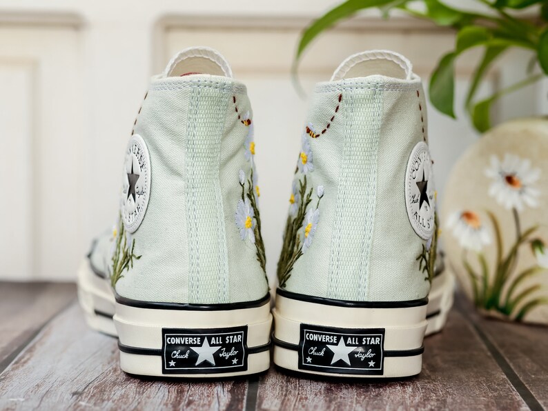 May include: A pair of light green high-top Converse sneakers with embroidered flowers and the text "Converse All Star Chuck Taylor" on the side.
