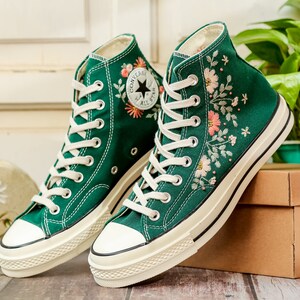 May include: A pair of green high-top canvas sneakers with white soles and floral embroidery. The sneakers have white laces and a black Converse logo on the side.