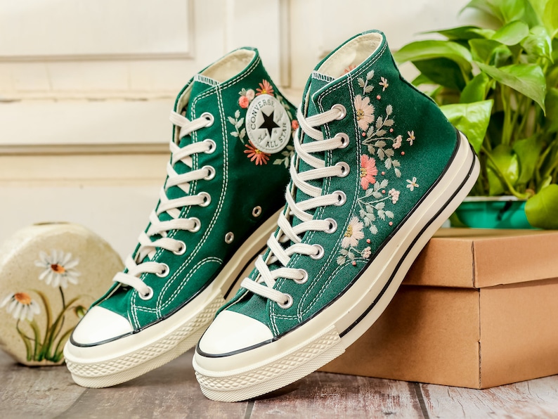 May include: A pair of green high-top canvas sneakers with white soles and floral embroidery. The sneakers have white laces and a black Converse logo on the side.
